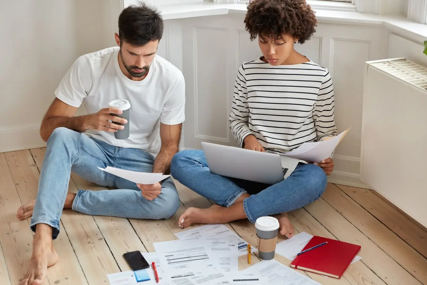 People, business, and work concept. A woman and a man who are coworkers review documentation and consider a productive strategy to raise profits, posing on a wooden floor with takeaway coffee and serious looks.